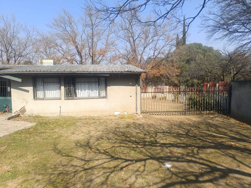 Rear view of the property showing a single-story structure with metal security bars, corrugated roofing, and a fenced yard area.