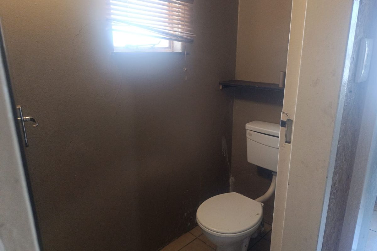 A small, dated bathroom featuring a standard toilet, tiled flooring, and a window, currently requiring cosmetic updates and wall repairs.