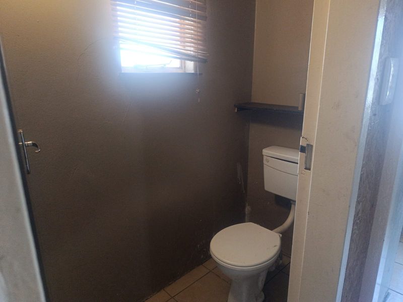 A small, dated bathroom featuring a standard toilet, tiled flooring, and a window, currently requiring cosmetic updates and wall repairs.