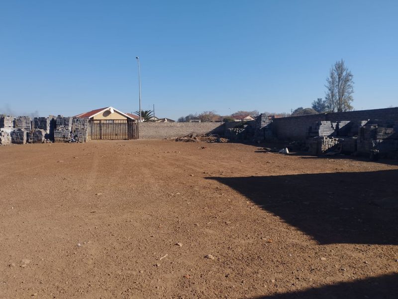 A large, undeveloped outdoor plot featuring a perimeter wall and metal gate, offering significant potential for landscaping or future development.