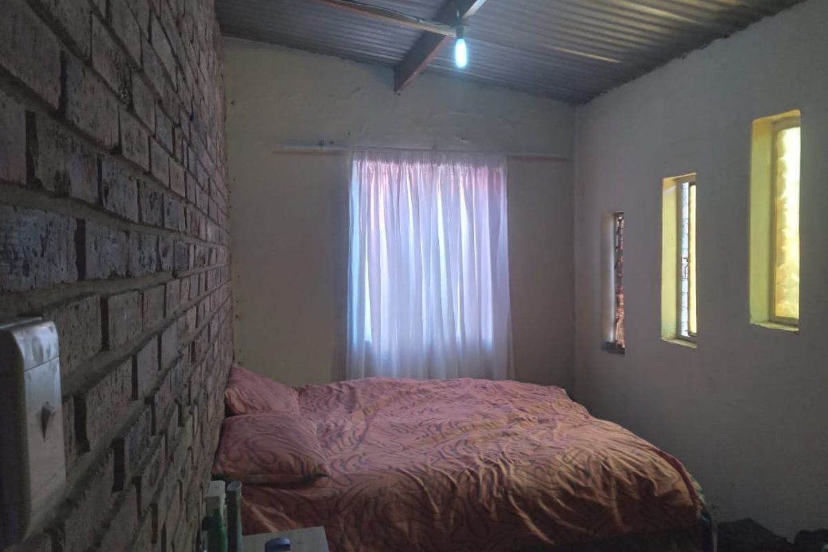 A bedroom featuring an exposed brick feature wall, corrugated metal ceiling, and unique vertical slit windows, offering a rustic industrial aesthetic.