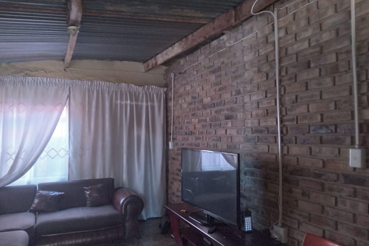 Living room featuring an exposed brick wall, corrugated metal ceiling with timber beams, and tiled flooring.