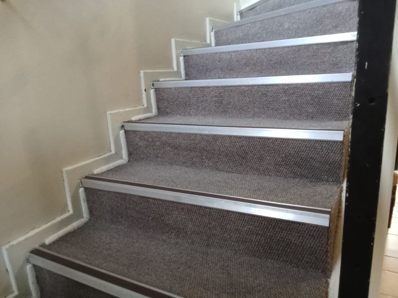 A staircase featuring grey carpeting and metal stair nosing, showing signs of wear and dated finishes.