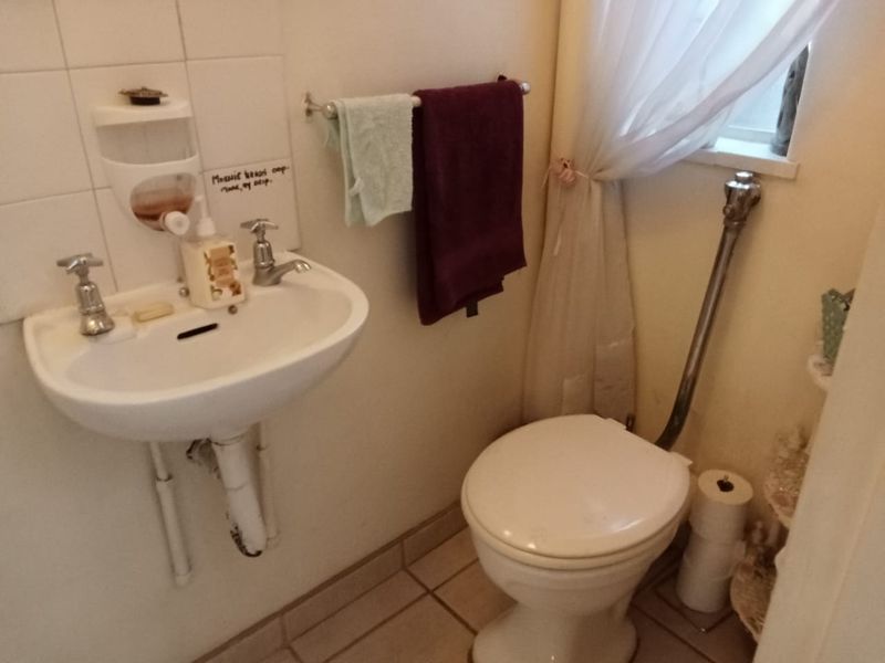 A compact bathroom featuring a wall-mounted basin and a standard flush toilet with tiled flooring and wall finishes.