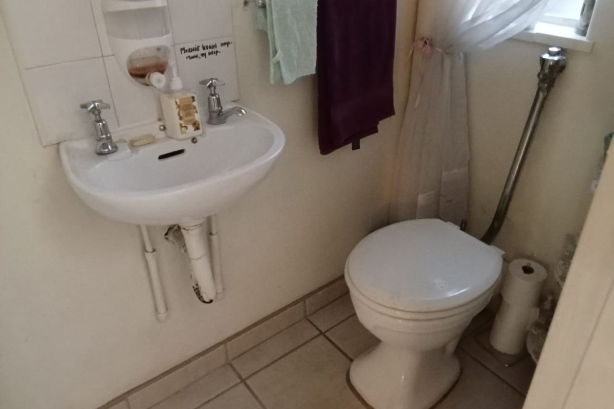 A compact bathroom featuring a wall-mounted basin and toilet with tiled flooring and splashback, requiring minor cosmetic updates.
