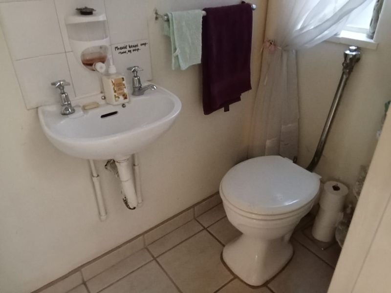 A compact bathroom featuring a wall-mounted basin and toilet with tiled flooring and splashback, requiring minor cosmetic updates.