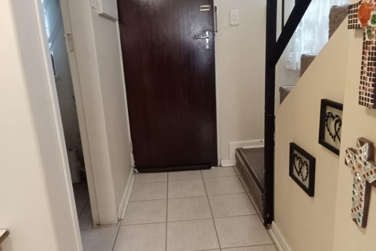 Entryway featuring tiled flooring and a staircase with a metal handrail, leading to an internal door and adjacent utility space.