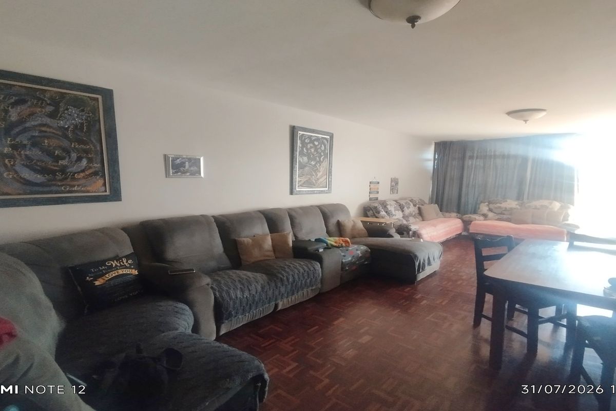 Spacious open-plan living and dining area featuring traditional parquet flooring and natural light from the adjacent balcony.