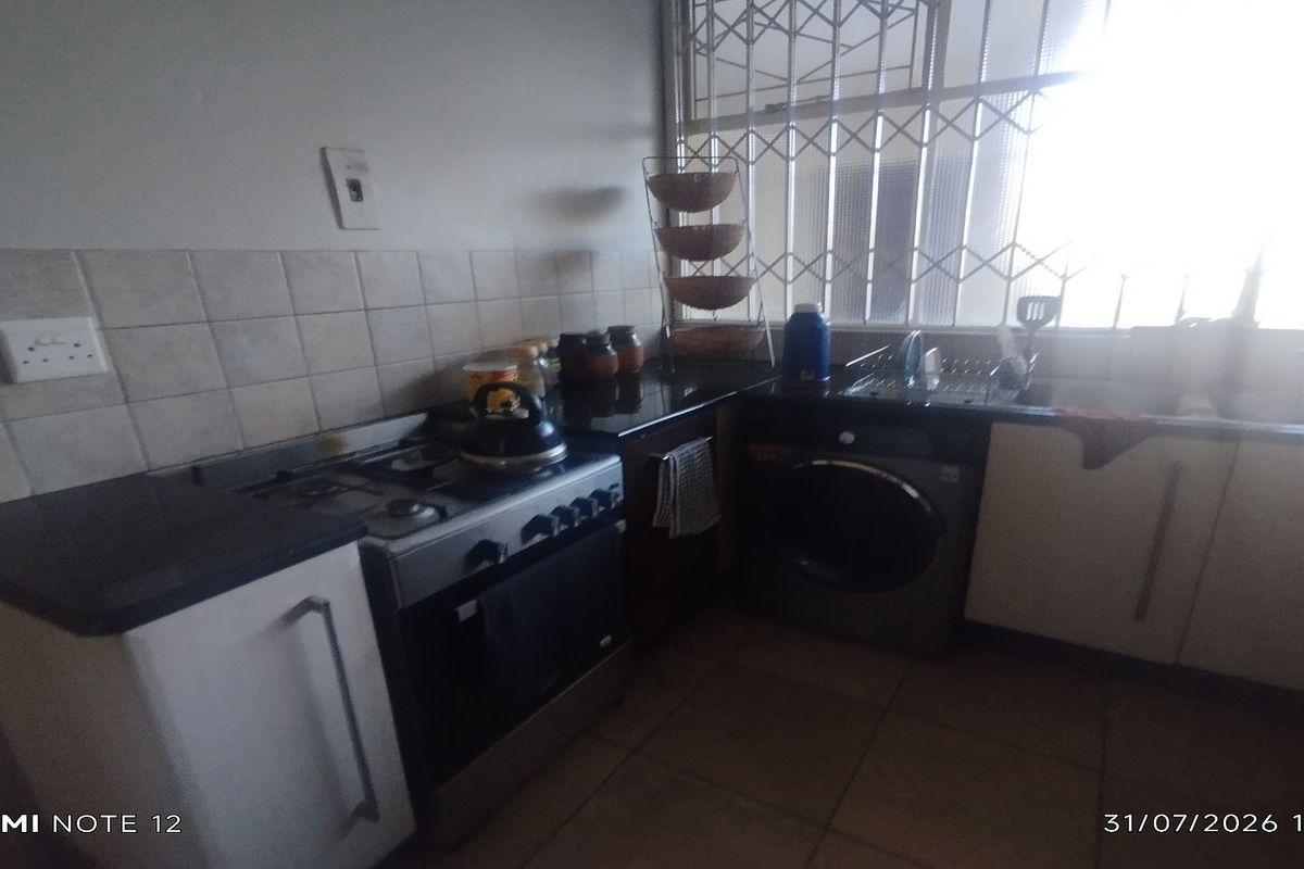 A functional kitchen featuring built-in cabinetry, tiled backsplash, a freestanding stove, and an integrated washing machine, with a security gate over the window.