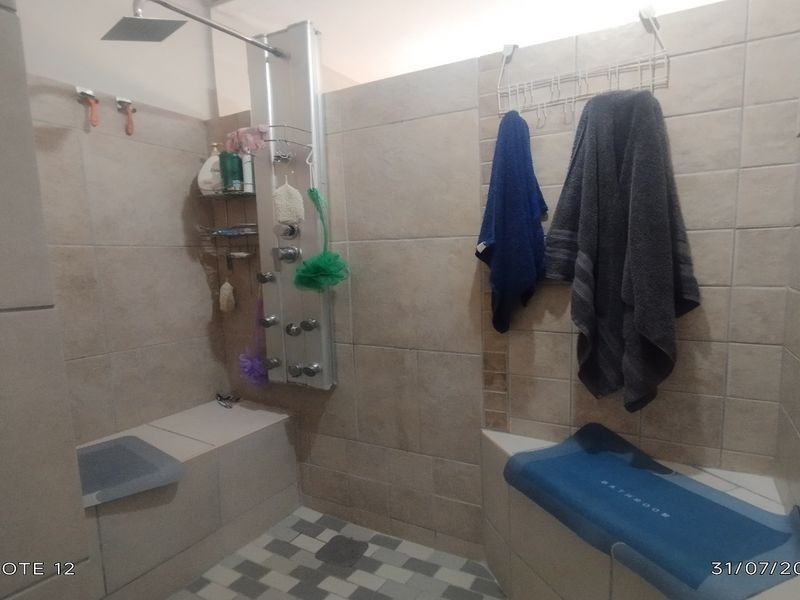 A bathroom shower area featuring a modern shower panel with rainfall head and built-in tiled seating benches.