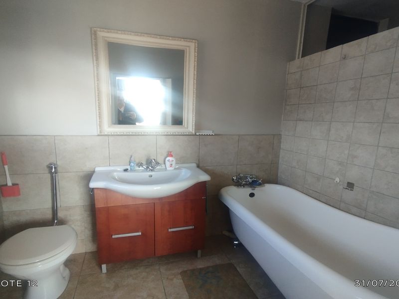 A functional bathroom featuring a vanity cabinet with basin, a freestanding bathtub, and neutral wall tiling.