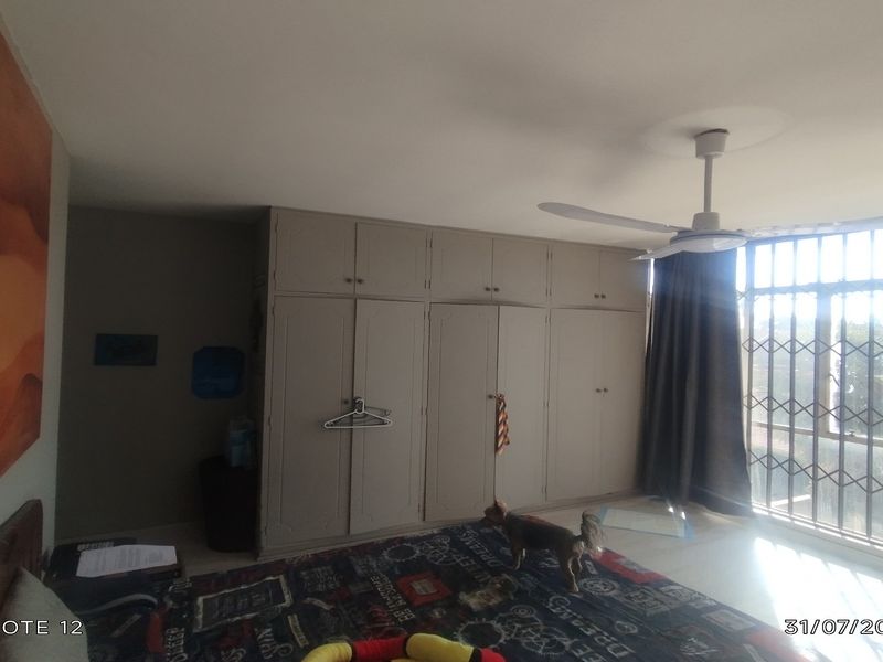 A bedroom featuring built-in cupboards, a ceiling fan, and a large window with security bars, providing natural light and storage space.