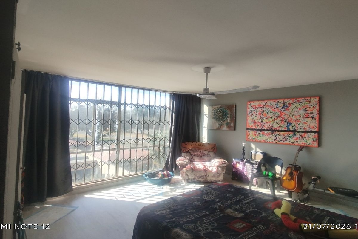 A bedroom featuring a ceiling fan, large window with security gate, and neutral wall finishes.