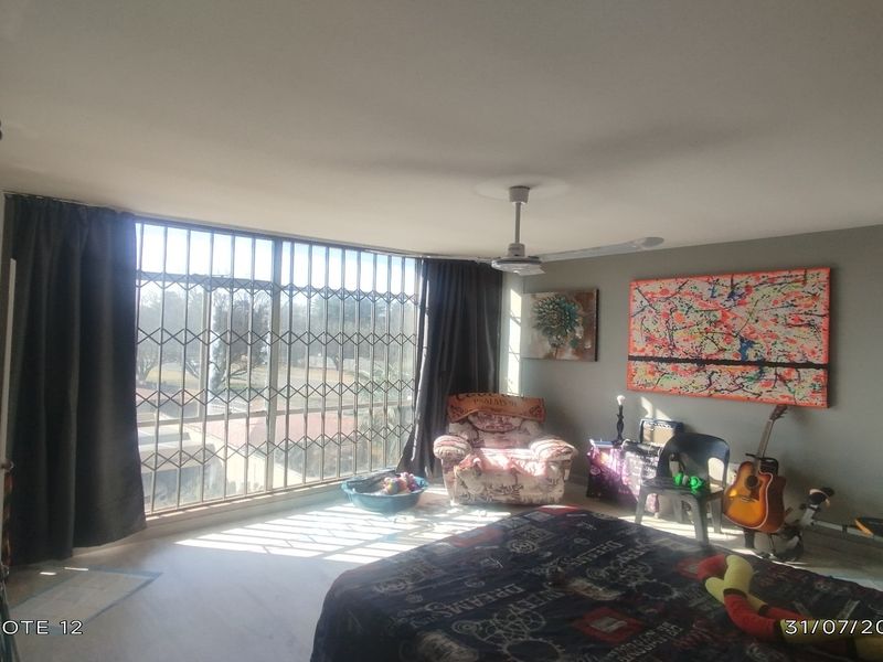 A bedroom featuring a ceiling fan, large window with security gate, and neutral wall finishes.