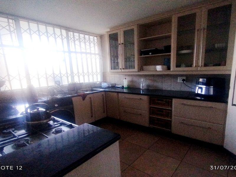 A functional kitchen featuring built-in cabinetry, granite countertops, a gas hob, and large windows with security bars, offering ample storage and workspace.