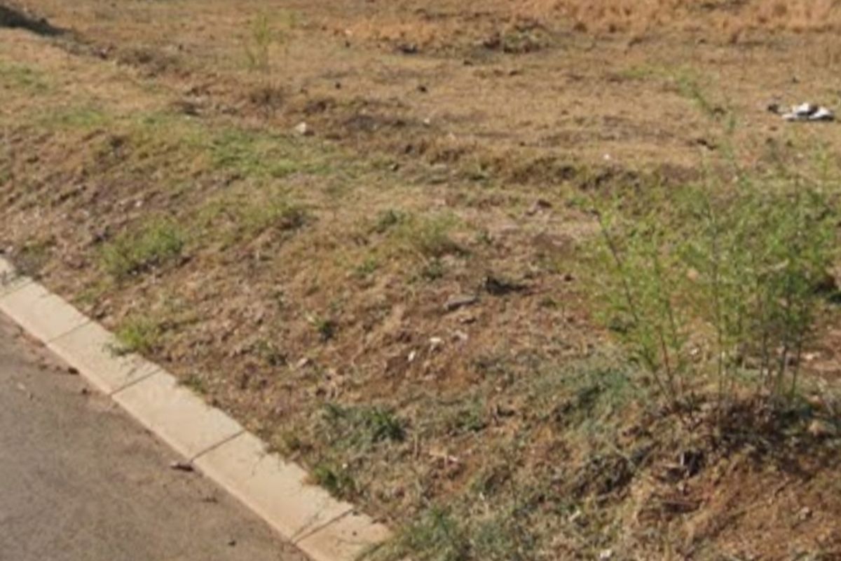 A vacant residential plot featuring a level surface, concrete kerbing along the street edge, and a perimeter boundary wall at the rear.
