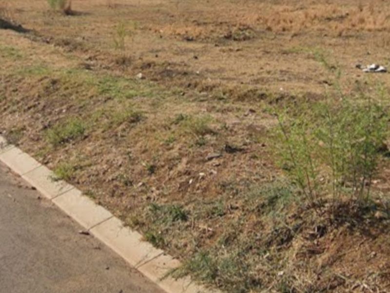 A vacant residential plot featuring a level surface, concrete kerbing along the street edge, and a perimeter boundary wall at the rear.