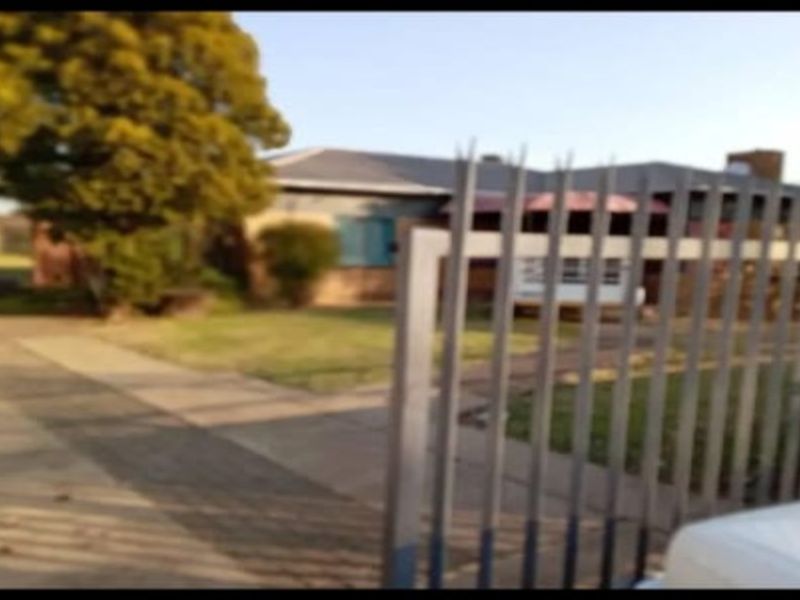Front view of a residential property featuring a metal security gate, concrete driveway, and brick exterior facade.