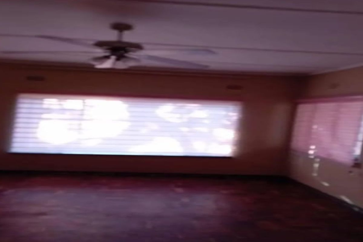 An empty living room featuring parquet flooring, a ceiling fan, and windows fitted with security burglar bars.