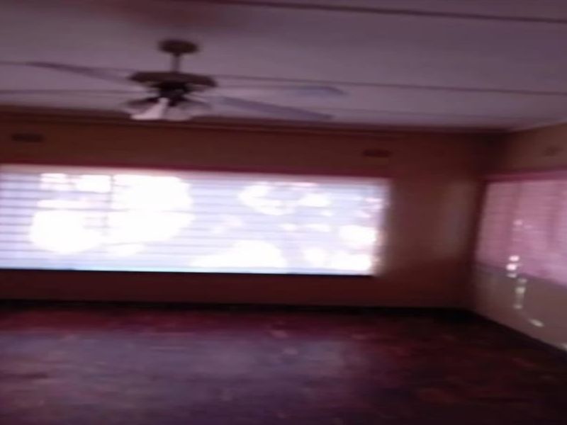 An empty living room featuring parquet flooring, a ceiling fan, and windows fitted with security burglar bars.