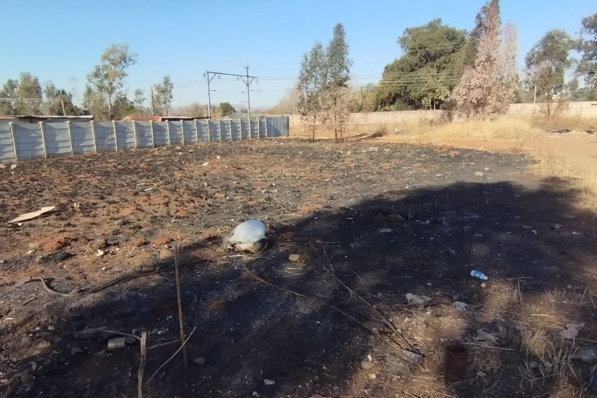 A vacant residential plot featuring a precast concrete boundary wall and scorched ground surface.