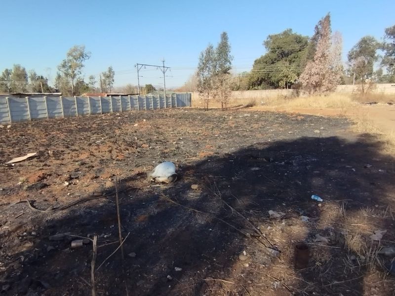 A vacant residential plot featuring a precast concrete boundary wall and scorched ground surface.