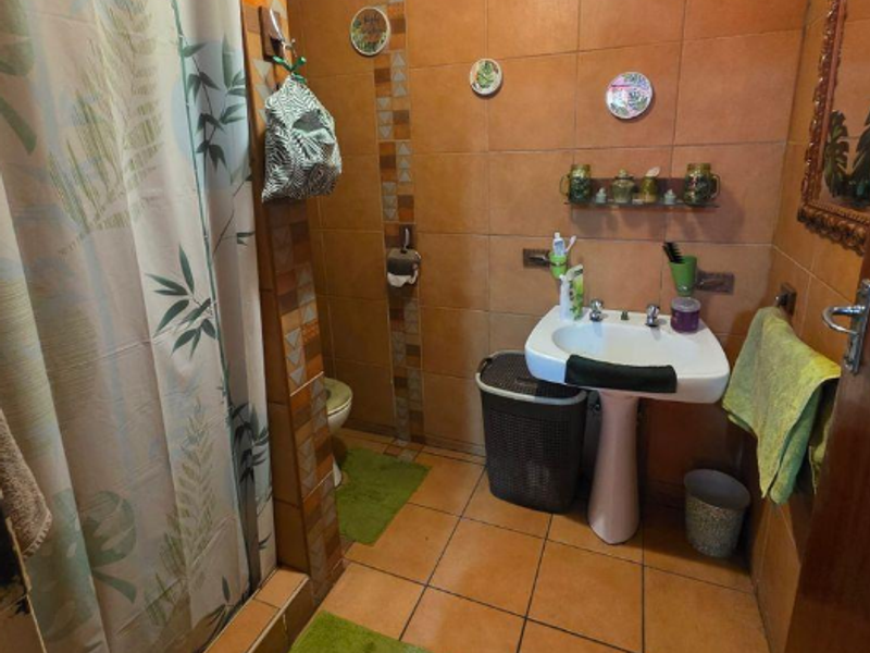 A functional bathroom featuring a pedestal sink, shower enclosure, and full-height wall tiling with a warm, earthy color palette.