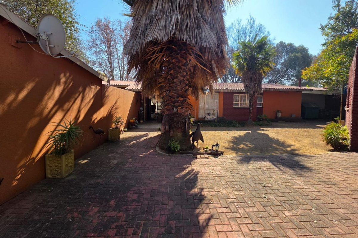 A rear exterior view of the property featuring a paved courtyard area, brick boundary walls, and established palm trees.