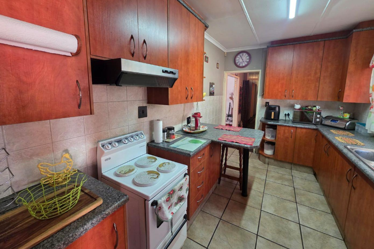 A functional kitchen featuring wooden cabinetry, tiled flooring, a tiled backsplash, and a freestanding stove with an extractor fan.