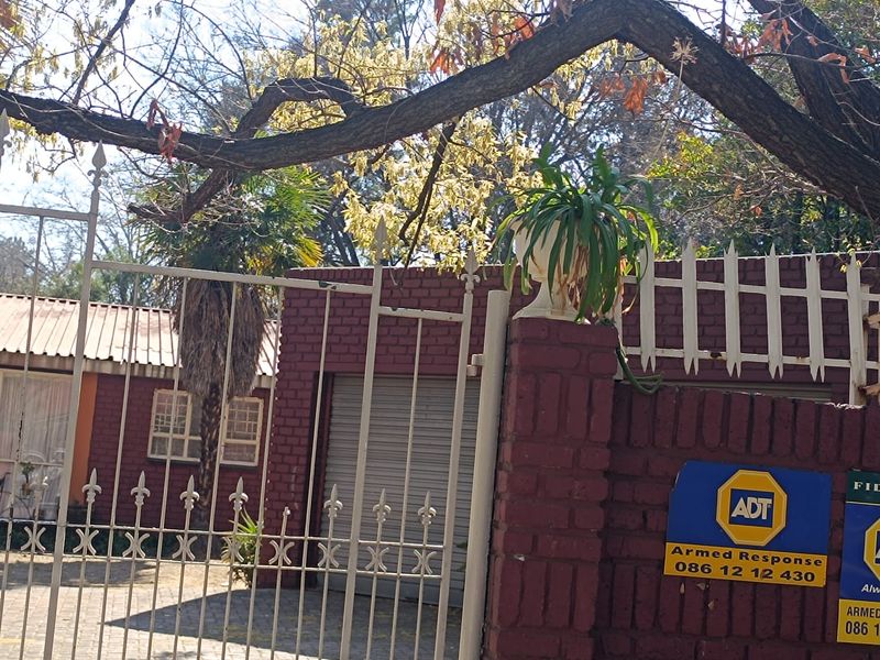 Front view of the property featuring a brick boundary wall, metal security gate, and paved driveway leading to a garage.