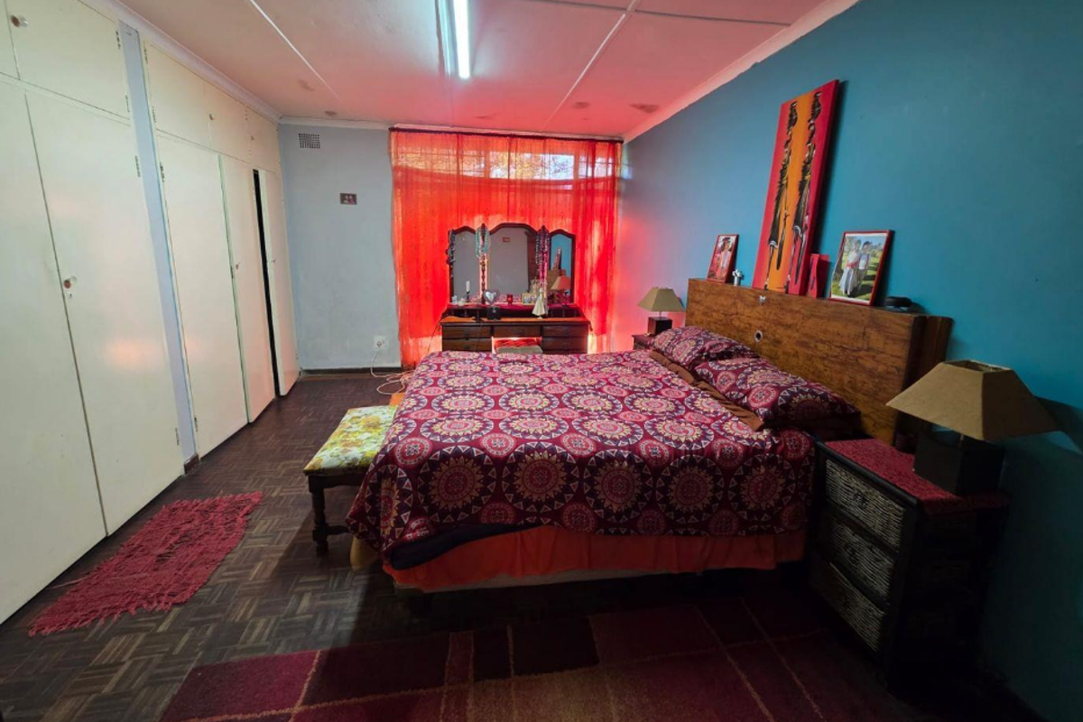Spacious bedroom featuring built-in cupboards, parquet flooring, and a large window with natural light.