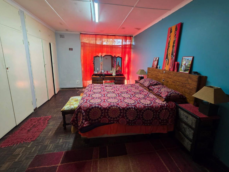 Spacious bedroom featuring built-in cupboards, parquet flooring, and a large window with natural light.