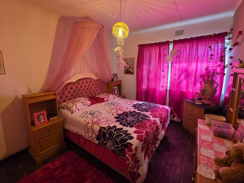A bedroom featuring parquet flooring and a ceiling ventilation vent, currently styled with vibrant pink decor and textiles.