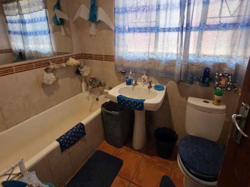 A functional bathroom featuring a pedestal basin, bathtub, and toilet with tiled walls and flooring, offering a classic layout ready for modernization.
