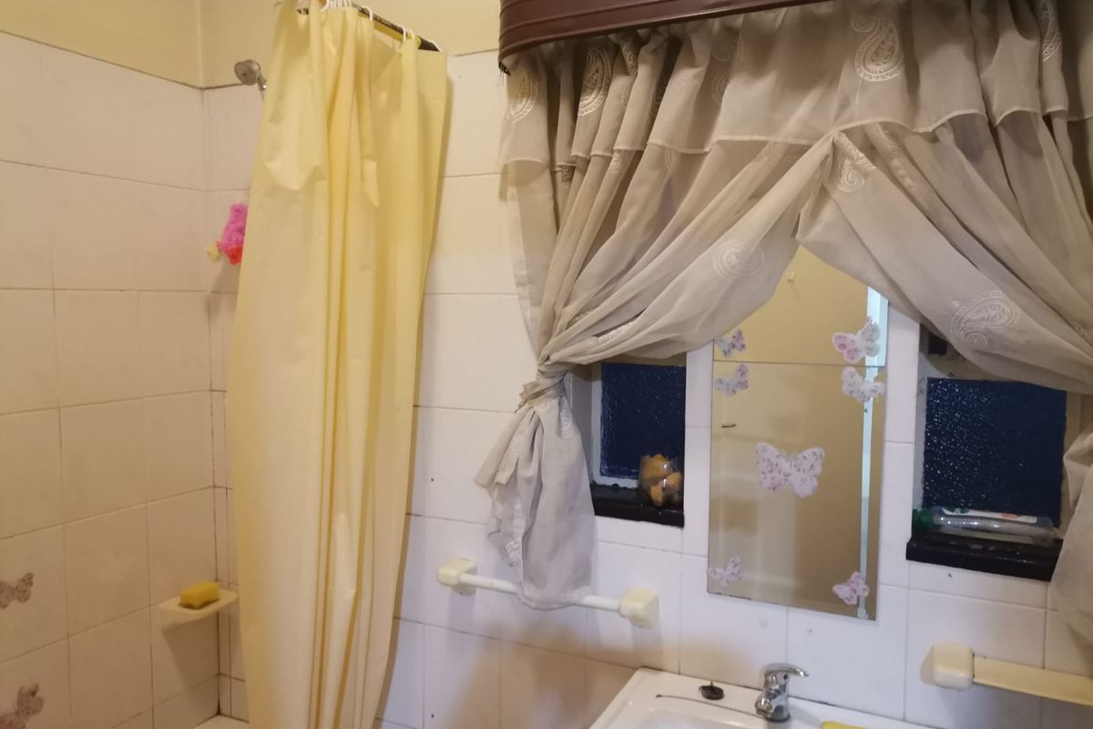 A dated bathroom featuring tiled walls, a wall-mounted basin with chrome mixer tap, and a shower area with a curtain rail.