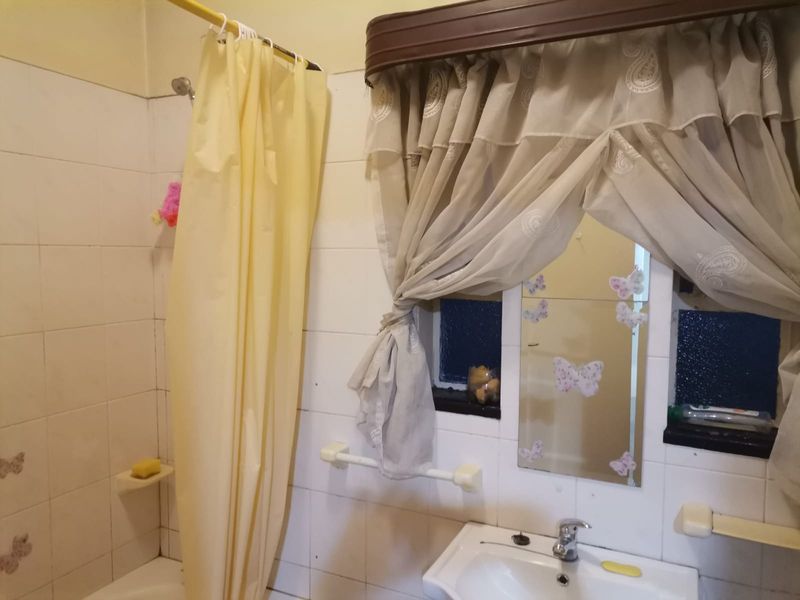 A dated bathroom featuring tiled walls, a wall-mounted basin with chrome mixer tap, and a shower area with a curtain rail.