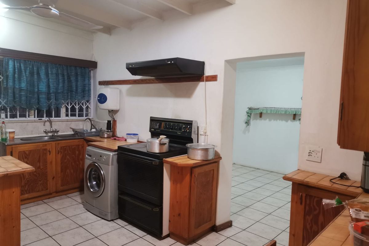A functional kitchen featuring wooden cabinetry, tiled flooring, and a built-in stove, with an adjacent utility area visible through the doorway.