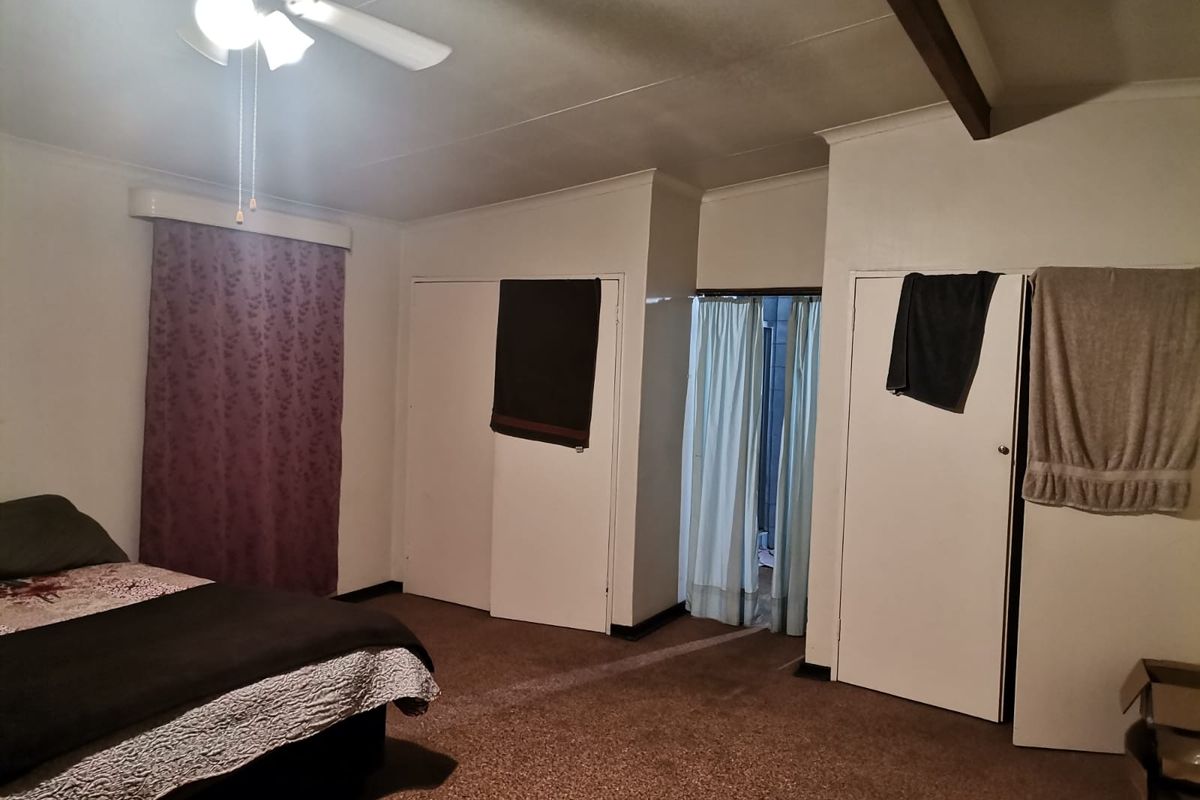 A bedroom featuring built-in cupboards, a ceiling fan, and carpeted flooring, offering a functional space with potential for cosmetic updates.