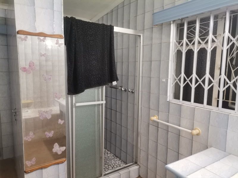 A functional bathroom featuring a shower enclosure, tiled walls, and a security gate on the window, offering a dated aesthetic ready for modernization.