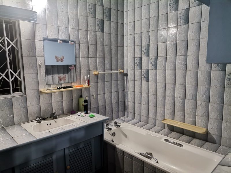 A functional bathroom featuring a built-in vanity, bathtub, and full-height wall tiling, offering potential for a modern renovation.