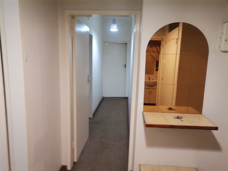A functional hallway featuring a built-in arched mirror with a tiled shelf, leading to internal rooms with carpeted flooring.