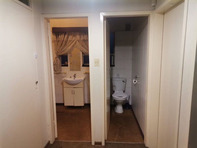 A functional bathroom area featuring a separate toilet and vanity basin with tiled walls and original flooring, offering potential for modernization.