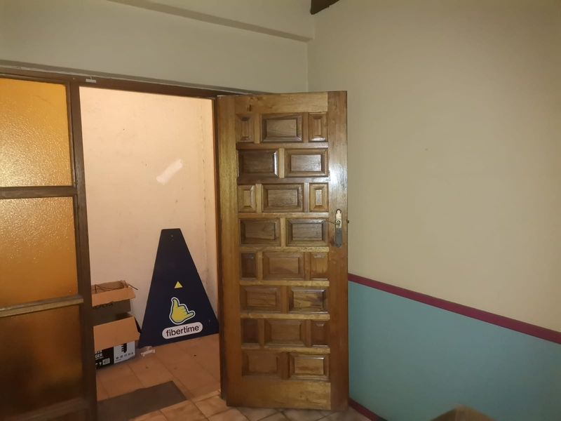 A view of a hallway featuring a solid wooden panelled door and tiled flooring, showing signs of wear on the walls.