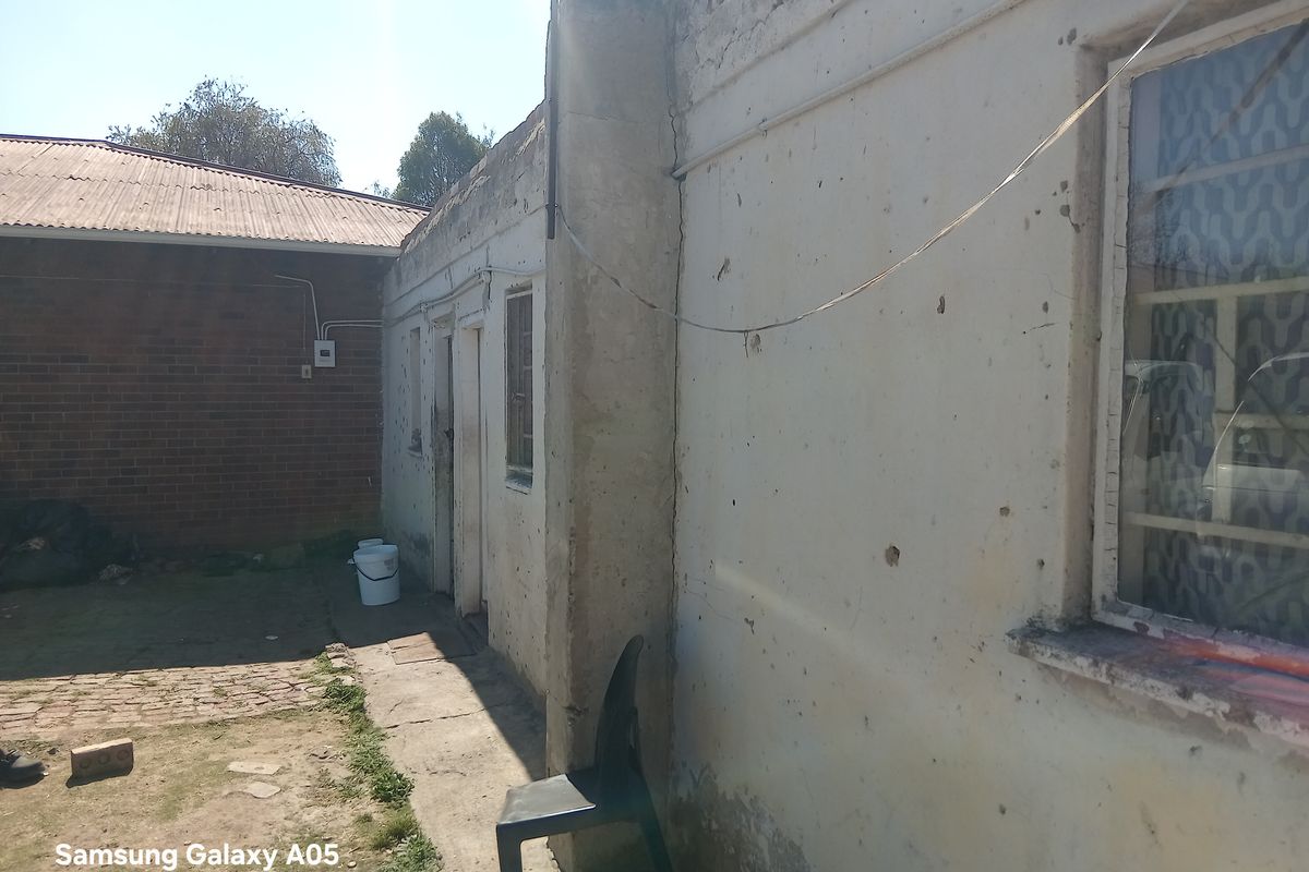 Rear exterior view of the property showing weathered brick and plastered walls, steel window frames, and a concrete pathway requiring maintenance.