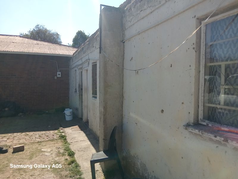 Rear exterior view of the property showing weathered brick and plastered walls, steel window frames, and a concrete pathway requiring maintenance.
