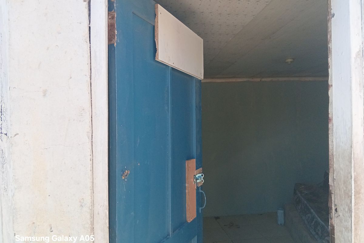 An interior view of an entrance doorway featuring a blue timber door leading into an empty room with tiled flooring and visible wall wear.