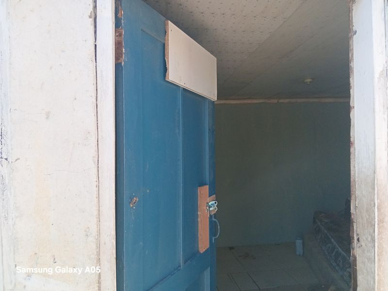 An interior view of an entrance doorway featuring a blue timber door leading into an empty room with tiled flooring and visible wall wear.