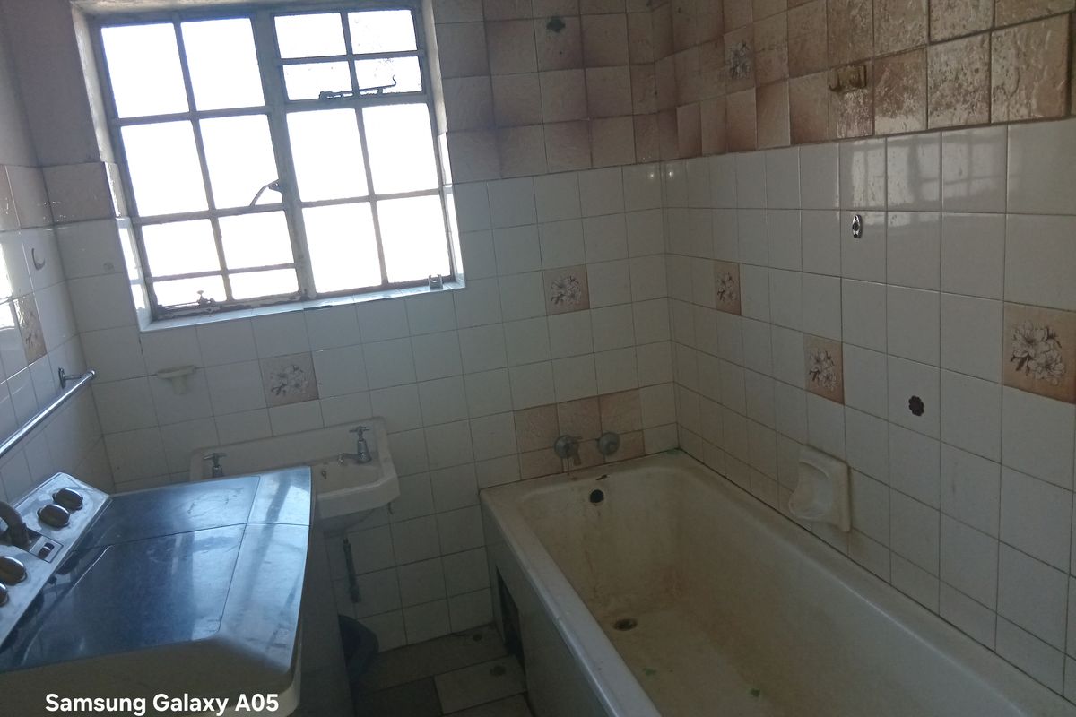 A dated bathroom featuring a bathtub, wall-mounted basin, and tiled finishes, requiring significant renovation and cosmetic updates to improve its condition.
