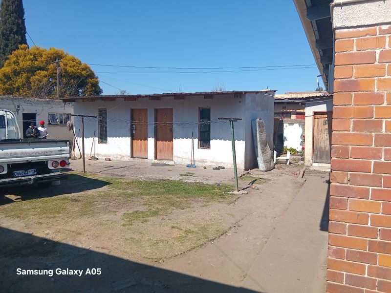 Rear exterior view of a basic outbuilding structure with exposed brick and plaster finishes, featuring multiple external access doors and a concrete yard area.