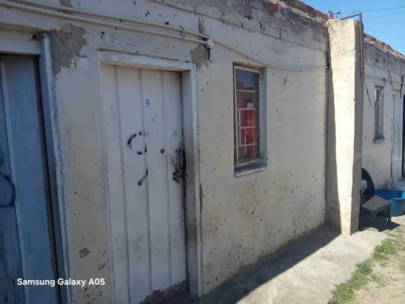 Exterior view of a residential building showing weathered plaster walls, a metal security door, and window security bars.